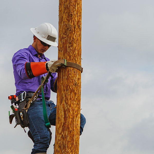 photo of an electrical lineworker student in safety gear, climbing an electrical pole